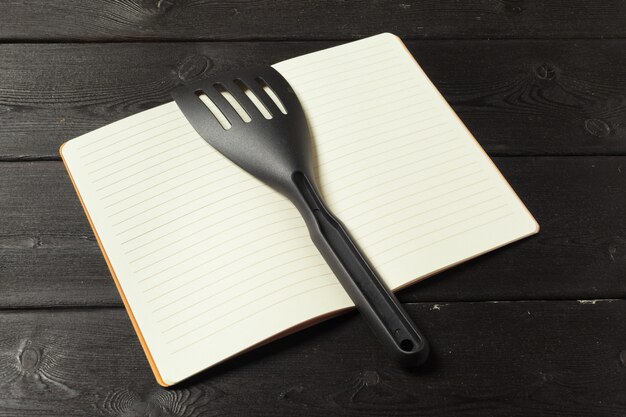 Feuille blanche de bloc-notes ouvert et d'ustensiles de cuisine sur la table avec une nappe, espace de copie