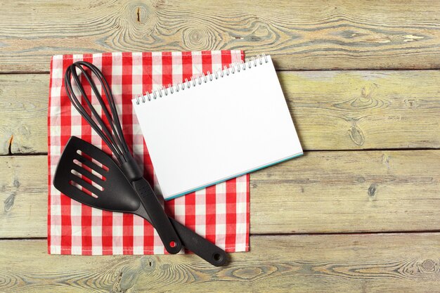 Feuille blanche de bloc-notes ouvert et d'ustensiles de cuisine sur une table avec une nappe