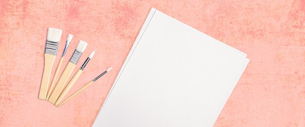 Une feuille blanche propre et des pinceaux sur un fond rose texturé avec un espace pour copier.