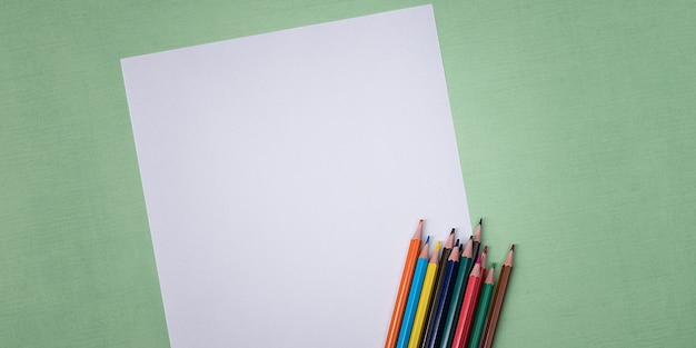 Une feuille blanche vierge et des crayons de couleur pour dessiner sur un fond texturé uni avec de l'espace
