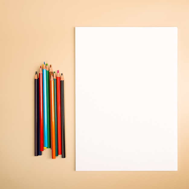Une feuille blanche vierge et des crayons de couleur pour dessiner sur un fond texturé uni avec de l'espace