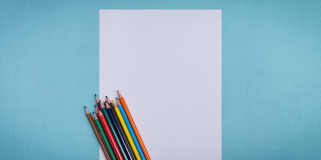 Une feuille blanche vierge et des crayons de couleur pour dessiner sur un fond texturé uni