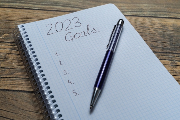 Feuille de cahier écrite 2023 pour mettre les résolutions et objectifs de l'année avec un stylo et un fond en bois