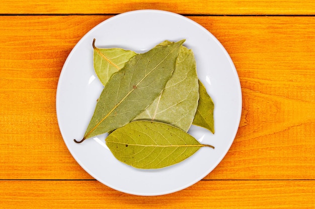 Photo feuille de laurier feuilles de laurier sur une plaque blanche sur une table en bois orange épices culinaires