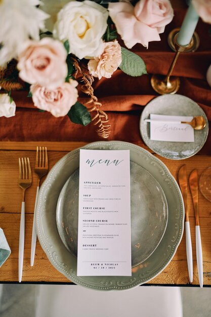 Une feuille avec un menu festif est sur une assiette à côté d'un bouquet de fleurs sur la table