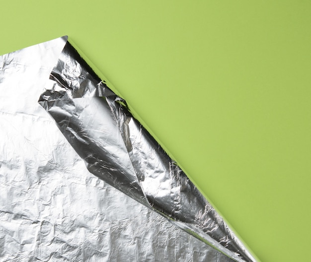 Feuille de papier d'aluminium roulée sur fond vert, le coin est plié, copiez l'espace