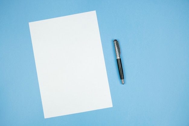 Feuille de papier blanc avec un stylo sur fond bleu.