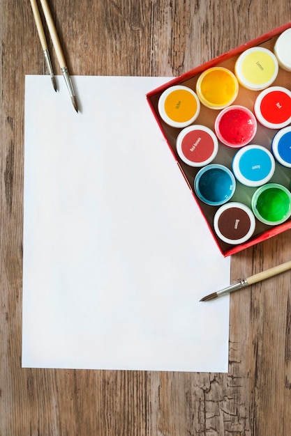 Feuille de papier blanc vide et boîte de peintures sur fond de bois