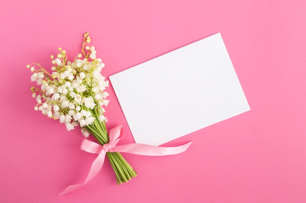 Feuille de papier blanc vierge et bouquet de muguets sur rose