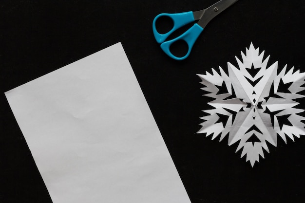 Feuille de papier flocon de neige ciseaux sur le fond noir