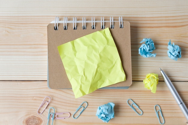 Une feuille de papier jaune sur un cahier avec un stylo et des morceaux de papier froissés sur une table en bois, une place pour la pâte.