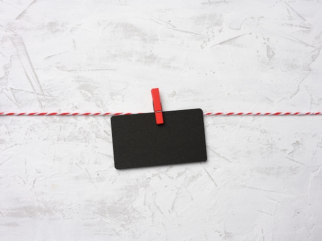 Feuille de papier rectangulaire en carton noir blanc accrocher sur des pinces à linge, fond de mur de ciment blanc