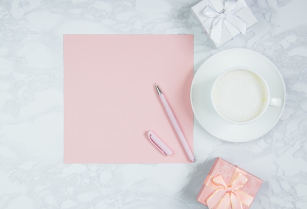 Feuille de papier rose, stylo rose, tasse de café et coffrets cadeaux sur la table