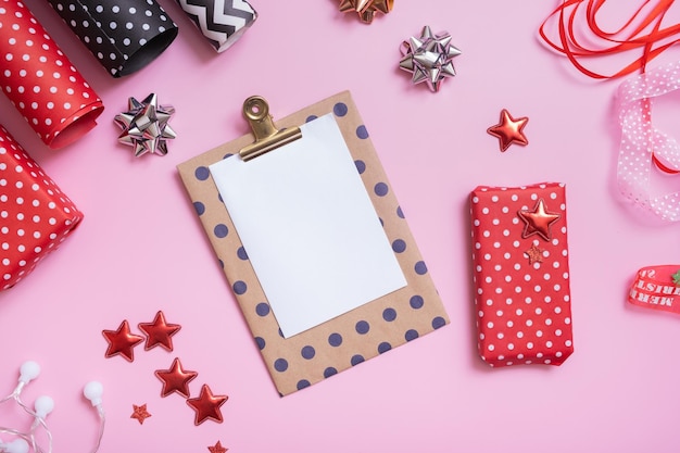 Feuille de papier vierge et cadeaux de noël avec du papier d'emballage à plat sur fond rose