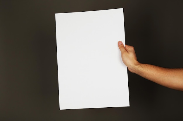 Feuille de papier vierge dans la main masculine sur fond sombre