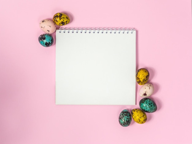 Une feuille de papier vierge entourée d'oeufs de pâques sur fond rose