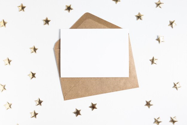 Feuille de papier vierge et enveloppe ouverte sur une table en bois blanche avec des confettis en forme d'étoile dorée