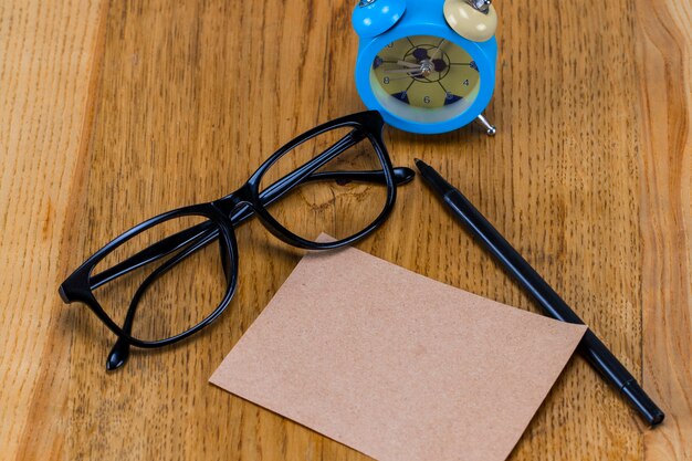 Feuille de papier vierge avec lunettes, réveil et stylo sur table en bois.