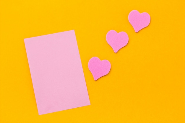 Feuille de papier vierge rose et coeurs roses sur un espace de copie de fond jaune