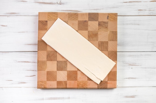 Une feuille de pâte crue sur une planche à découper dans une cage à pâte pour faire des croissants Fond en bois clair