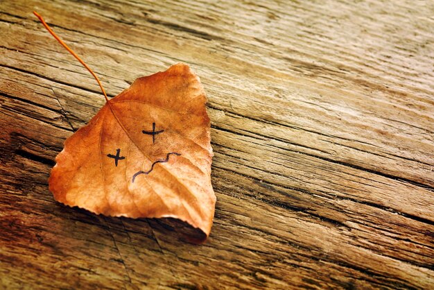 Feuille séchée brune avec une photo d'un visage triste sur le vieux fond en bois avec des fissures