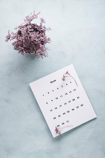 Feuille vierge du calendrier mensuel et bouquet de fleurs séchées sur la table. Planification et organisation du temps. Vue verticale