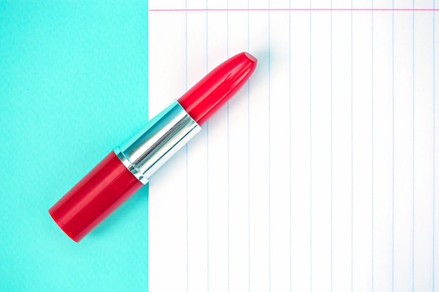 Une feuille vierge de papier pour ordinateur portable et rouge à lèvres sur fond bleu.