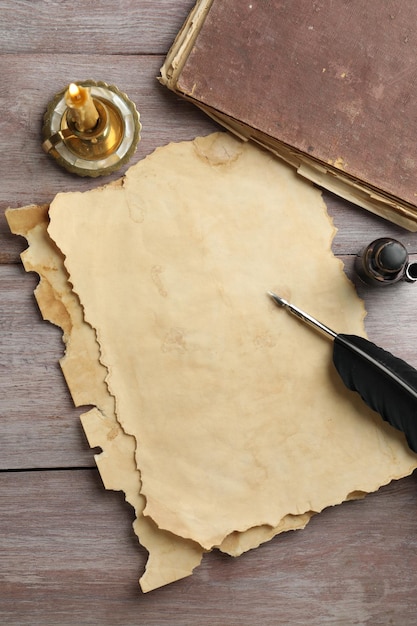 Une feuille de vieux papier parchemin, un encrier à plumes noires, un livre vintage et une bougie sur une table en bois.