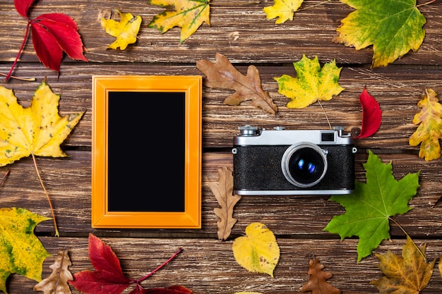 Feuilles d&#39;automne, caméra et cadre sur une table en bois.