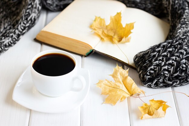 Feuilles d'automne jaune tasse de café écharpe tricotée chaude avec vieux livre ouvert sur des planches en bois