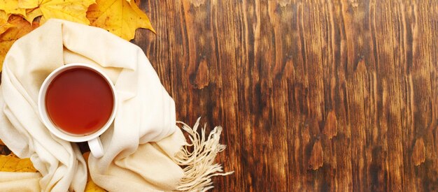 Feuilles d'automne avec une tasse de thé ou de café à côté d'une écharpe sur un fond en bois avec espace de copie