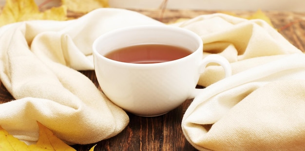 Feuilles d'automne avec une tasse de thé ou de café à côté d'une écharpe sur un fond en bois avec espace de copie