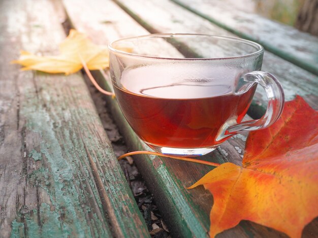 Feuilles d'automne et une tasse de thé chaude. Table en bois contre une froide journée ensoleillée sur un fond naturel.