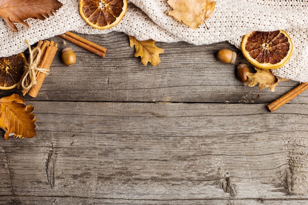 Feuilles, couverture tricotée, orange sec, cannelle et glands sur une vieille table en bois