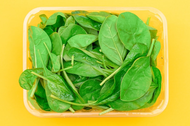 Feuilles d'épinards frais dans un emballage en plastique transparent sur fond jaune