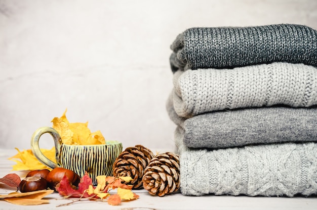 Feuilles d'érable jaune d'automne, pommes de pin, châtaignes et une tasse de thé à côté d'une pile de pulls d'hiver chauds et tricotés dans plusieurs nuances de gris sur fond gris. notion d'automne