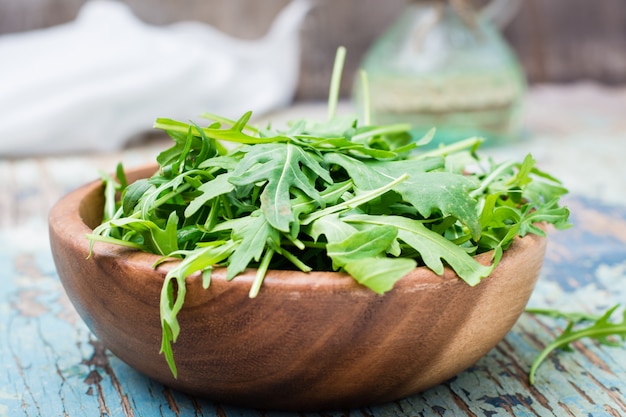 Feuilles fraîches de roquette dans un bol en bois, pichet d&#39;huile et serviette de table sur une table en bois