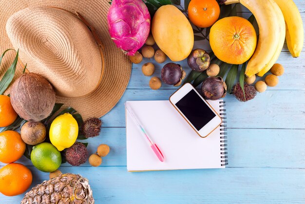 Feuilles de palmier tropical, chapeau, beaucoup de fruits sur un fond en bois bleu.