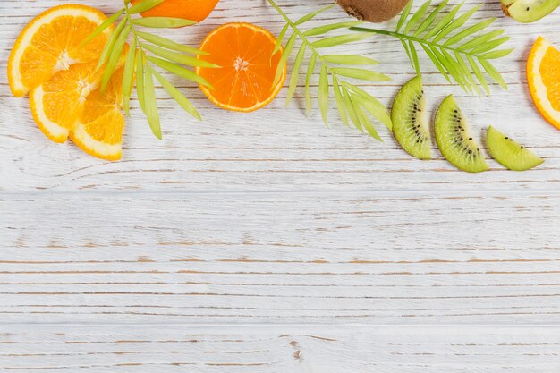 Photo feuilles de palmier vertes et tranches de fruits tropicaux frais sur une table en bois blanche