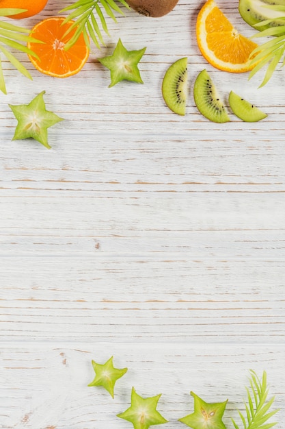 Feuilles de palmier vertes et tranches de fruits tropicaux frais sur une table en bois blanche