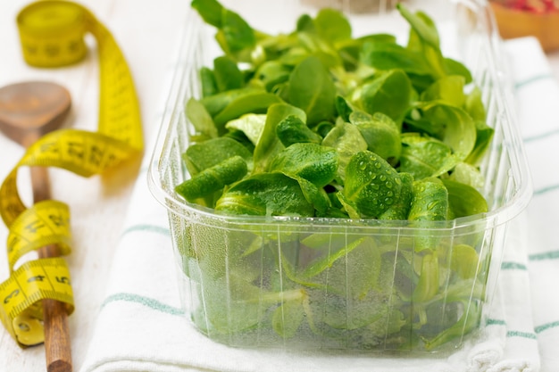 Feuilles de salade crue fraîche dans une boîte en plastique sur une table en bois clair. Mise au point sélective.