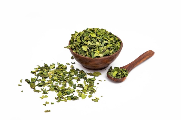 Feuilles sèches de neem ou Azadirachta indica dans un bol en bois sur fond blanc avec une cuillère en bois