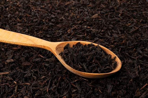 Feuilles de thé séchées dans une cuillère en bois sur fond de feuilles de thé ou de texture