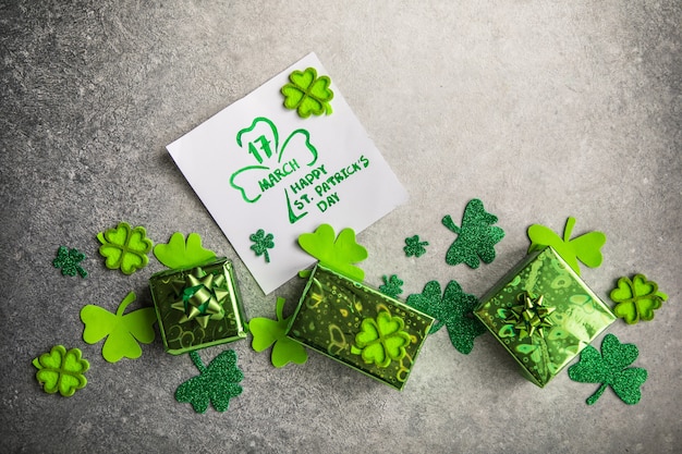 Feuilles de trèfle décoratives, boîte de cadeaux verte, pièces de monnaie sur fond de pierre, pose à plat. Célébration de la Saint-Patrick. Carte Joyeuse Saint-Patrick