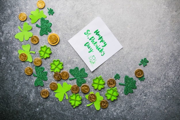 Feuilles de trèfle décoratives, boîte de cadeaux verte, pièces de monnaie sur fond de pierre, pose à plat. Célébration de la Saint-Patrick. Carte Joyeuse Saint-Patrick