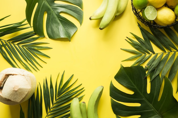 Feuilles tropicales, boisson à la noix de coco et fruits sur jaune. Vacances d'été. Espace pour le texte.