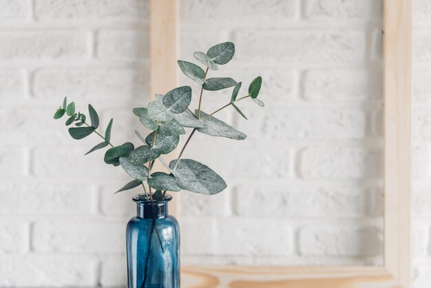 Feuilles vertes d'eucalyptus dans un vase bleu et un cadre photo en bois contre un mur de briques blanches Minimalisme de style scandinave.