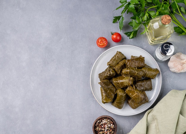 Feuilles de vigne farcies Dolma cuisine traditionnelle grecque turque du Caucase sur une assiette bleue avec des herbes fraîches sur un fond clair avec de l'huile d'olive tomate et poivre