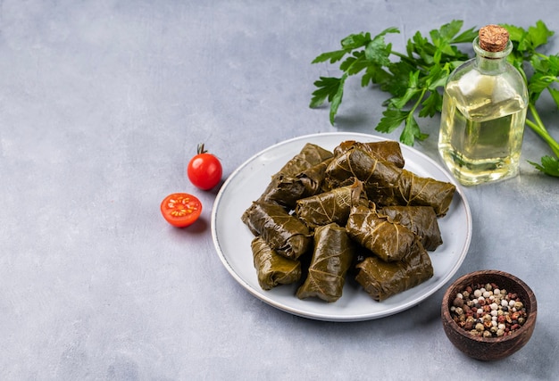 Feuilles de vigne farcies Dolma cuisine traditionnelle grecque turque du Caucase sur une assiette bleue avec des herbes fraîches sur un fond clair avec de l'huile d'olive tomate et poivre