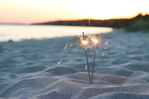 Feux de Bengale sur le sable près de la mer sur fond de coucher de soleil